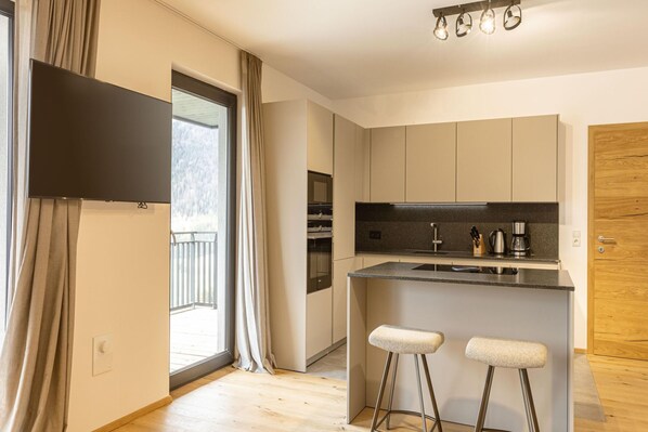 Eine moderne Küche mit einer großen Kücheninsel, Barhocker, einem Flachbildfernseher und einer Schiebetür zum Balkon.