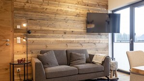 Una sala moderna con una pared de madera, un sofá gris, un televisor de pantalla plana y un ventanal con vistas.