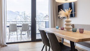 Et moderne spiseområde med et træbord, stole og en stor lampe. En vase med tørrede planter står på bordet, og et fjernsyn er monteret på væggen.