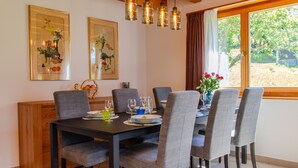 Ein Essbereich mit Holztisch, grau gepolsterten Stühlen und hängenden Pendelleuchten.