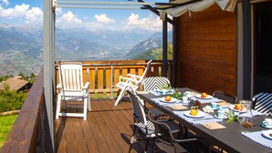Eine Holzdar Terrasse mit einem Essplatz, mit Blick auf eine gebirgige Landschaft.