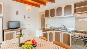 A kitchen with wooden cabinets, a stove, and a dining table with a fruit bowl. - Vento Alpino by Interhome (Valle di Non)