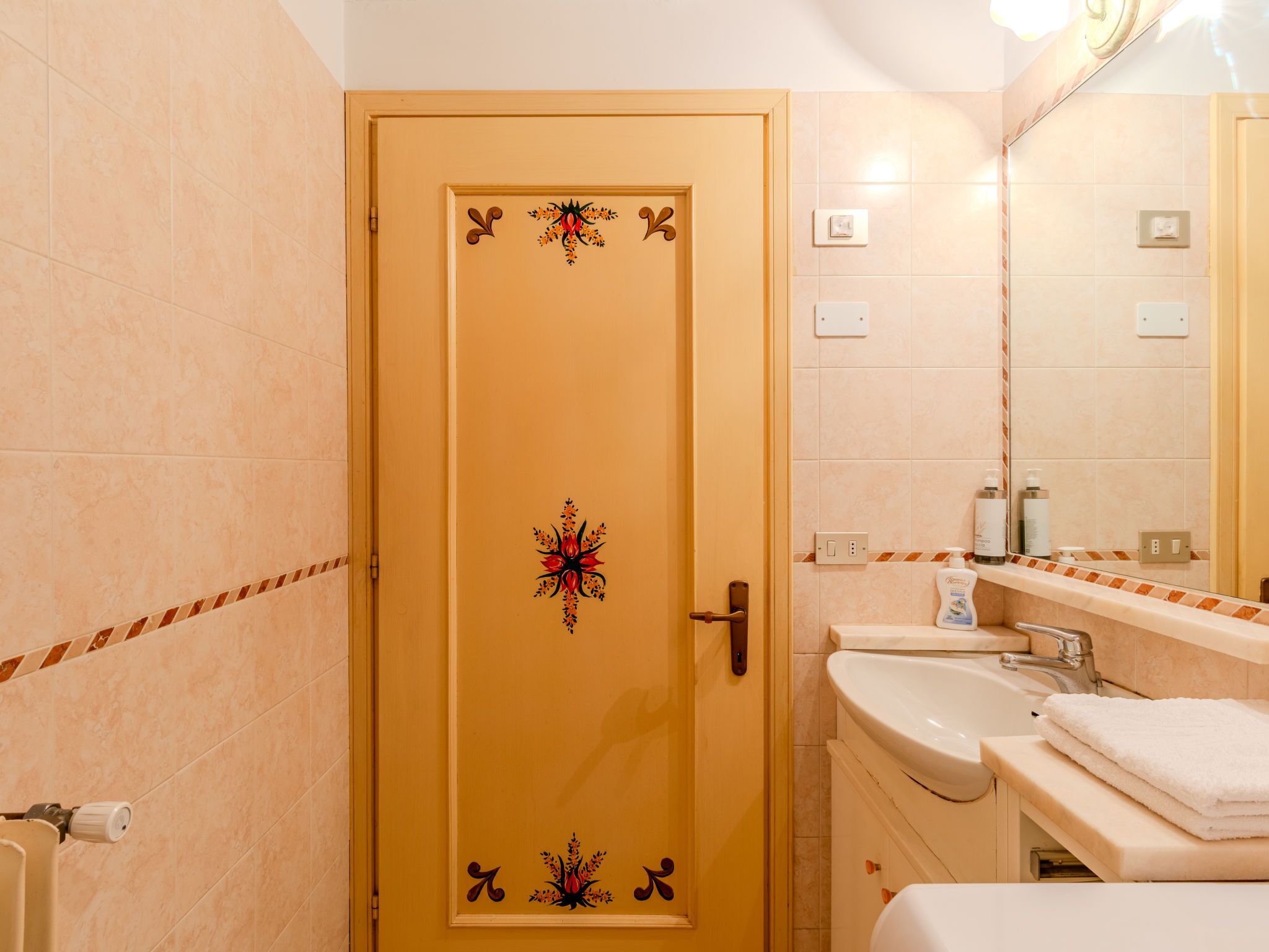 A bathroom with a beige door, a sink, a mirror, and a towel rack.