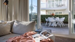 Un salon moderne avec un canapé, une table en verre et un magazine. Dehors, il y a un balcon avec un ensemble de mobilier de jardin et une vue sur un immeuble.