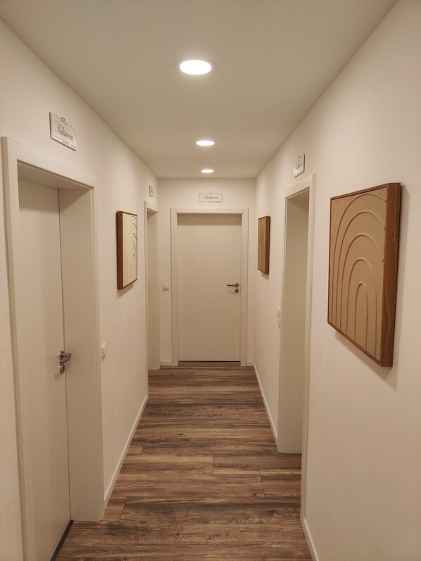 Een gang met houten vloer, witte muren en deuren met daarop 'Kidroom' en 'Slaapkamer'.