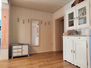 Una habitación con piso de madera, un armario blanco con puertas de cristal, un espejo en la pared y un pequeño mueble azul.