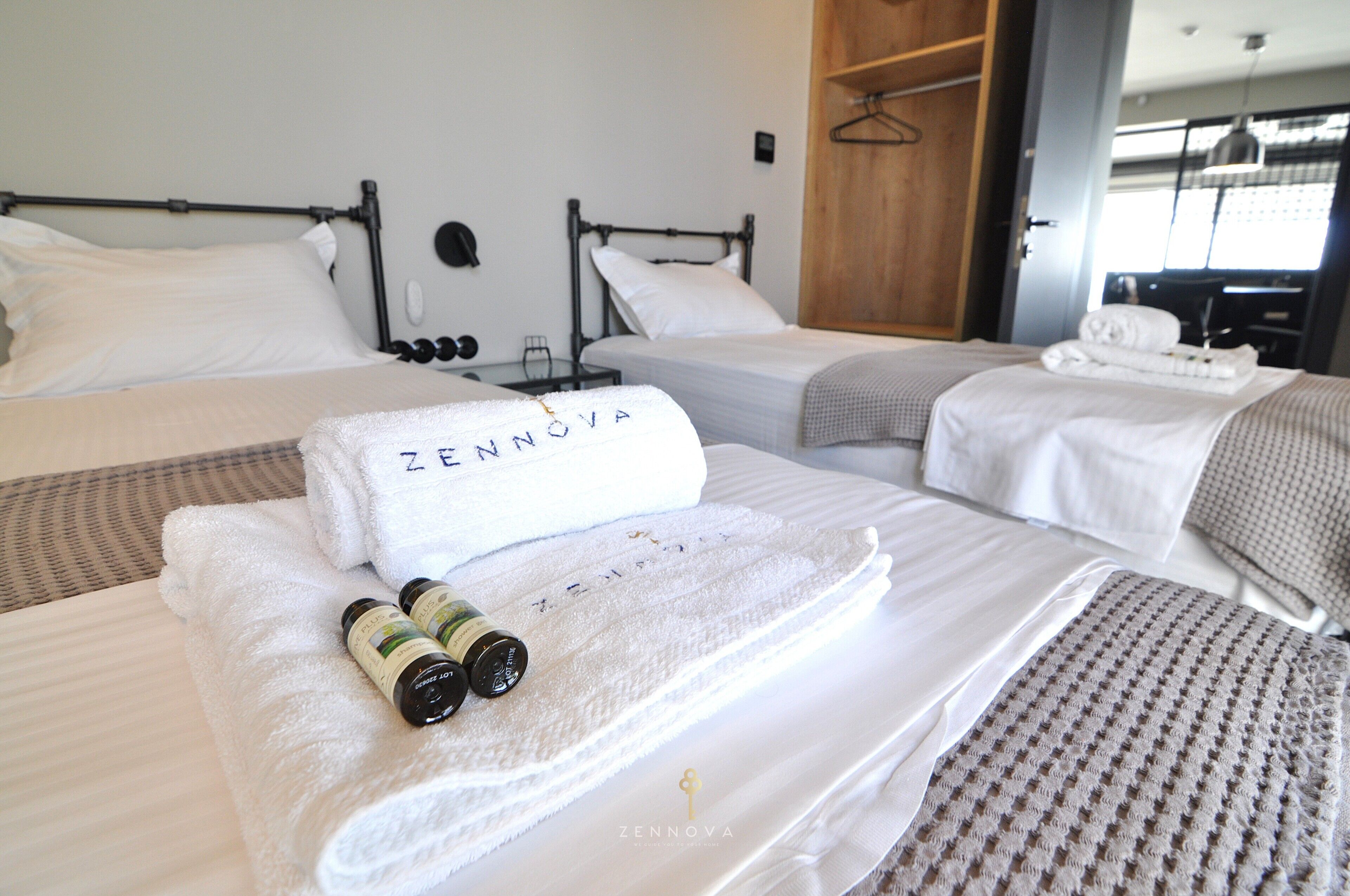 Une chambre d’hôtel avec deux lits, chacun agrémenté d’une serviette blanche soigneusement pliée et d’un flacon de lotion.