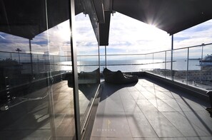 Um edifício alto com varanda de vidro, com vista para a água e para o horizonte da cidade.