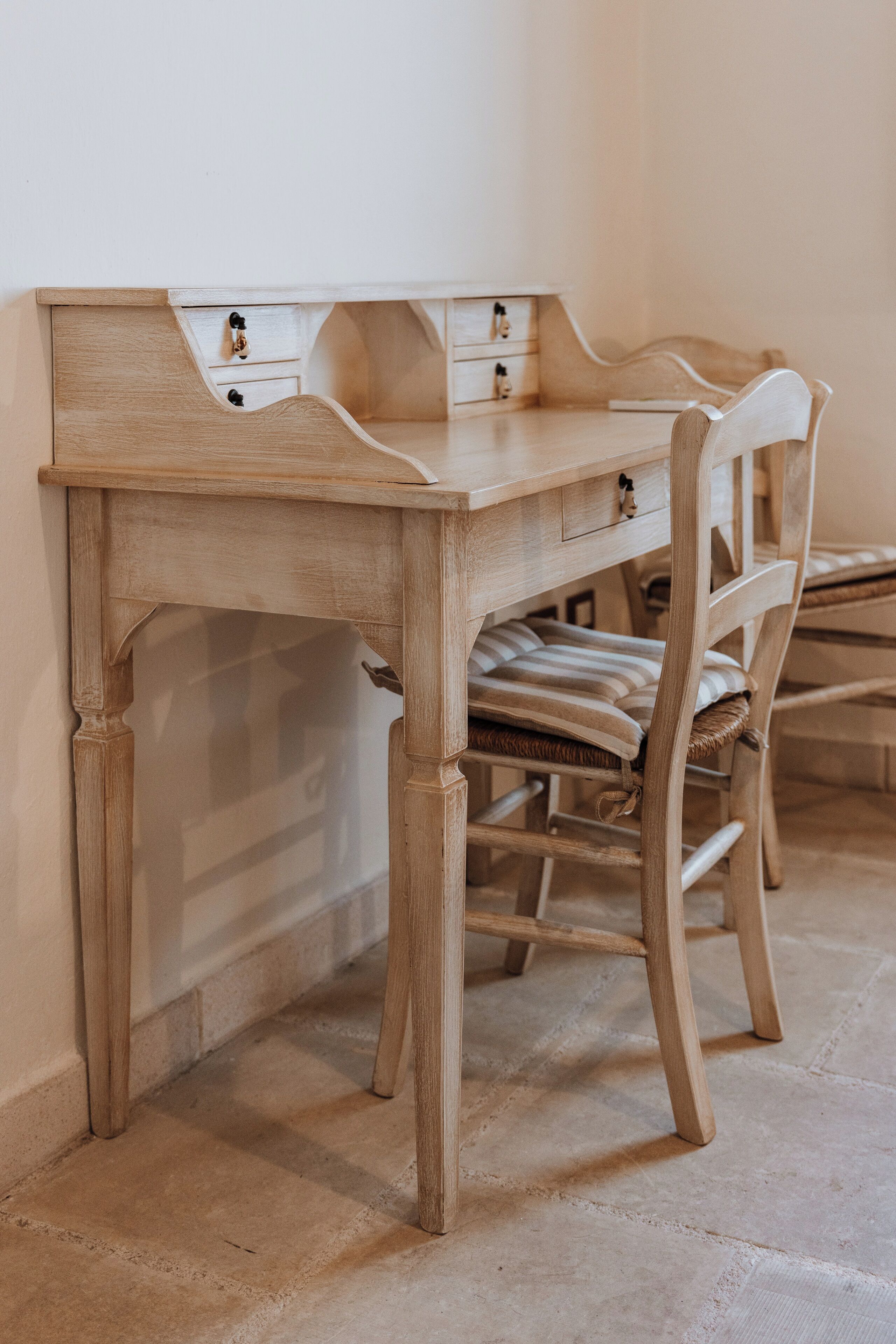 A wooden desk with drawers and a chair with a striped cushion.