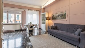 Un salon moderne avec un canapé gris, une table à manger avec des chaises, un meuble blanc et un tableau accroché au mur.