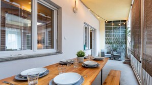 Un coin repas avec une table en bois dressée pour quatre personnes, de grandes fenêtres et une vue sur un jardin.