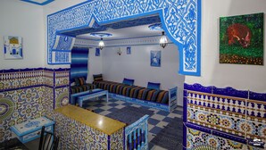 Een kamer met blauw-witte betegelde vloer, een zithoek, een bijzettafeltje en een schilderij van een stier.