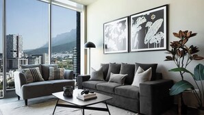 Ein modernes Wohnzimmer mit einem grauen Sofa, einem Couchtisch und einem großen Fenster mit Blick auf die Stadt.
