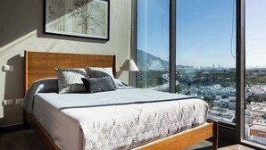 Ein Schlafzimmer mit großem Fenster, einem Bett mit gemusterten Betttextilien und einem gerahmten Bild an der Wand.