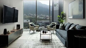 A modern living room with a large TV, comfortable seating, a coffee table, and a view of a mountainous landscape. - Mountain View in Valle Poniente, Rooftop Pool, Gym (Santa Catarina)