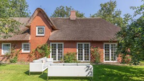 Ein Haus mit einem Strohdach, Ziegelwänden und einem weißen Korbsessel im Vorgarten.