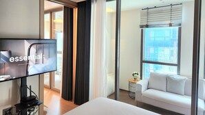 A modern hotel room with a bed, a TV, a sofa, and a large window offering a city view. - ThePlace34 (Busan)