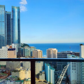 A cityscape with modern high-rise buildings, a view of the sea, and a Ferris wheel.