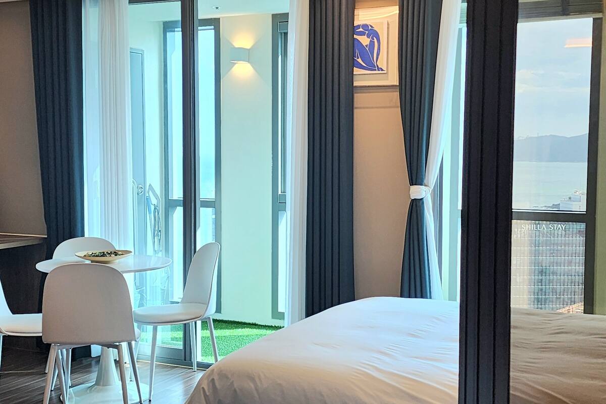 A hotel room with two beds, a dining area with a table and chairs, and a balcony with a view of the sea.