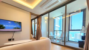 A modern hotel room with a large window, a flat-screen TV mounted on the wall, a white sofa, and a small table. - ThePlace34 (Busan)