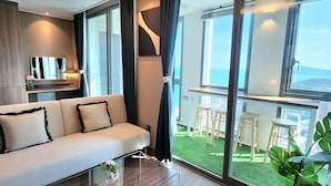 A modern living room with a sofa, a glass coffee table, and a view of a balcony with outdoor seating. - ThePlace34 (Busan)