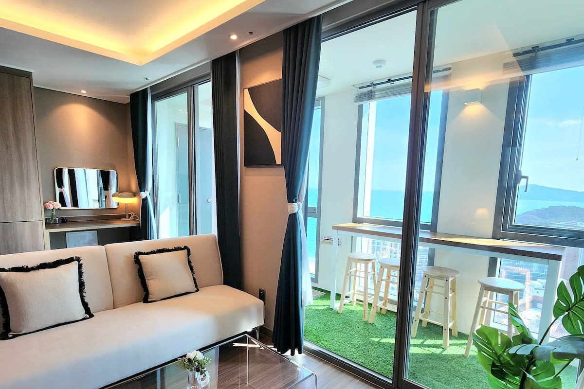 A modern living room with a sofa, a glass coffee table, and a view of a balcony with outdoor seating.