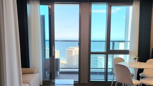 A modern hotel room with a large balcony, a dining area, and a view of the city and sea. - ThePlace34 (Busan)