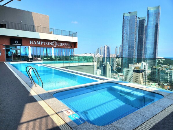 A rooftop pool with a city view, a Hampton Coffee building, and modern high-rise buildings in the background.