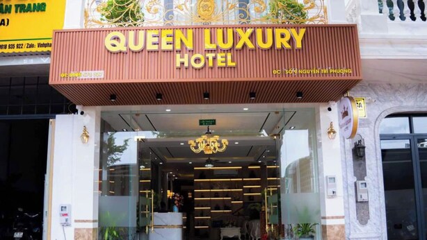 L’entrée de l’hôtel Queen Luxury, avec son design moderne, se distingue par sa façade en verre, un balcon décoratif et un lustre.