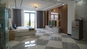 Une chambre d’hôtel moderne avec un sol à carreaux, un lit agrémenté d’une touche de bleu, une télévision, un réfrigérateur et une grande fenêtre avec des rideaux.