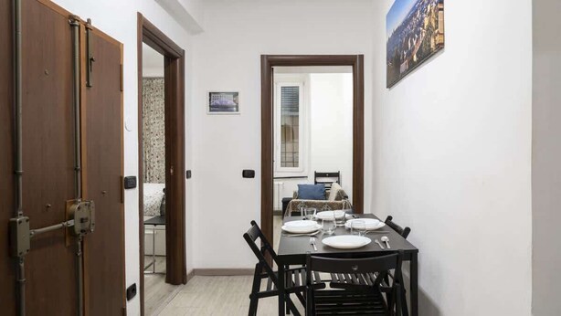 Un comedor con una mesa dispuesta para cuatro, una puerta de madera y un cuadro en la pared.