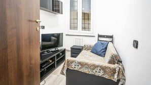 Una habitación pequeña con cama, televisión y ventana.