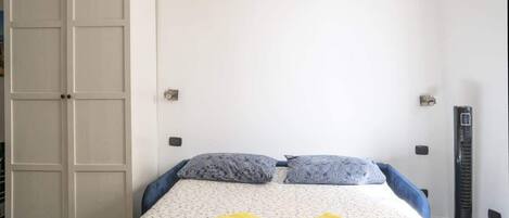 Une chambre à coucher avec un lit, deux oreillers, un radiateur et une armoire.