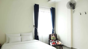 Et hotelværelse med seng, stol, bord med bakke med mad og en vægmonteret ventilator.