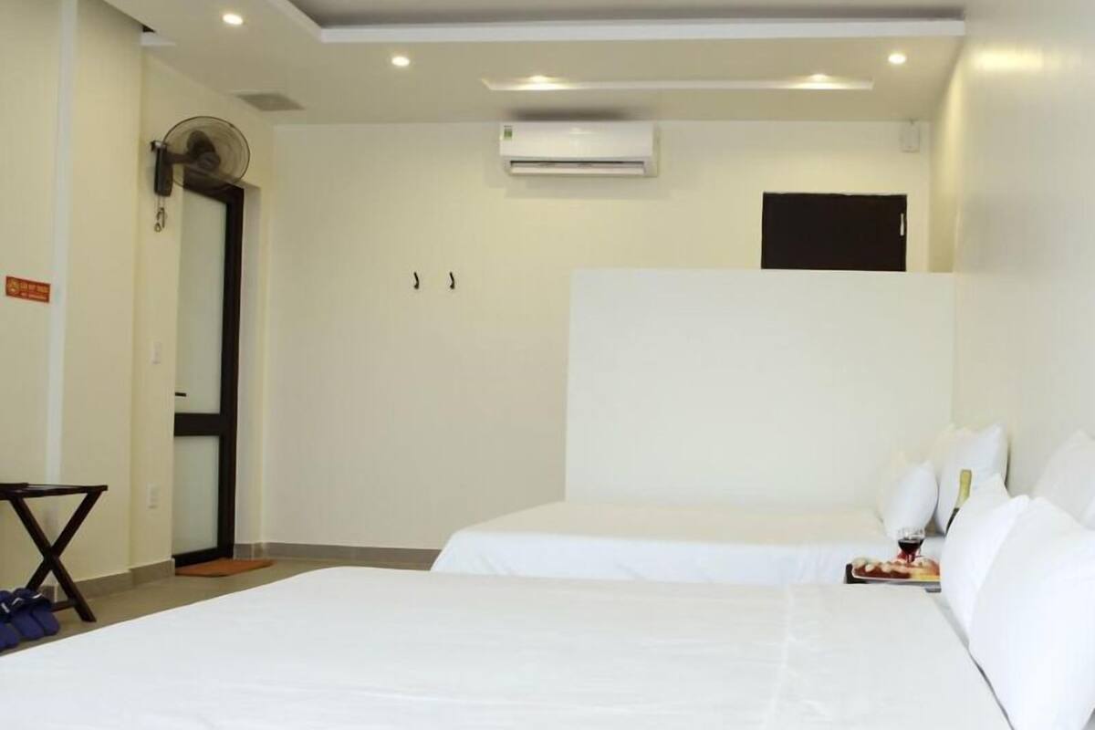 A hotel room with two beds, a ceiling fan, an air conditioning unit, and a small table with a book and a glass of wine.