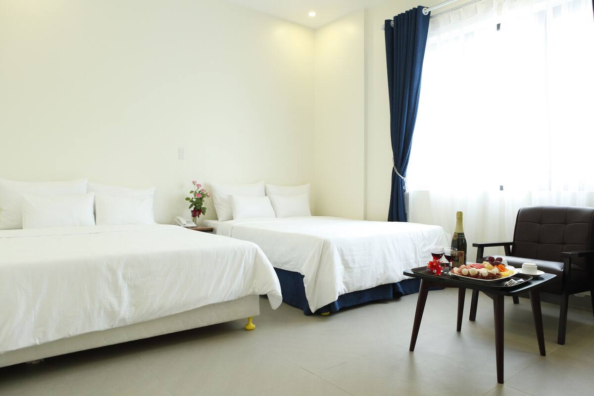 A hotel room with two beds, a dining table with a bottle, glasses, and a plate of food.