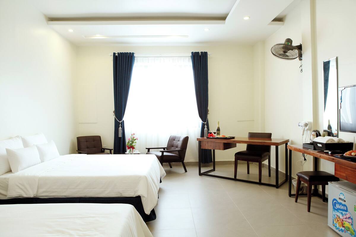 A hotel room with two beds, a desk with a chair, a TV, and a minibar.