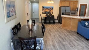 A dining area with a covered table and chairs, a kitchen with wooden cabinets, and a blue sofa.