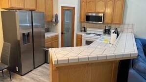 A compact kitchen with wooden cabinets, a stainless steel refrigerator, a microwave, and a stove.