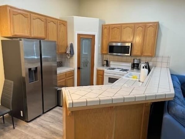 A compact kitchen with wooden cabinets, a stainless steel refrigerator, a microwave, and a stove. - Charming 3-bedroom house with AC and WiFi in welcoming Frazier Park (Frazier Park)