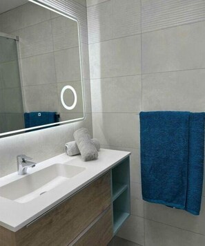 A modern bathroom with a large mirror, a sink, and a blue towel hanging on the wall.