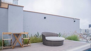 Een terras op het dak met een zwembad, een rieten bank en een houten tafel met stoelen.