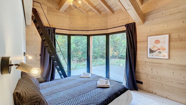 Ein Schlafzimmer einer Holzhütte mit einem Bett, einer Leiter und einem großen Fenster.