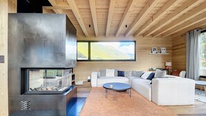 Ein modernes Wohnzimmer mit Kamin, Holzboden und großen Fenstern mit Blick auf eine reizvolle Landschaft.