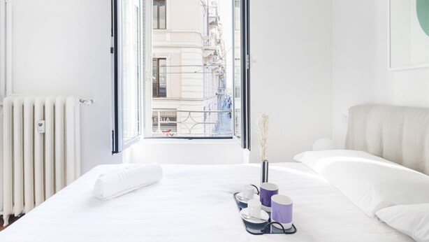 A hotel room with a bed, a radiator, a window, and a view of buildings outside. - Easylife - A touch of design in Porta Venezia (Milano)