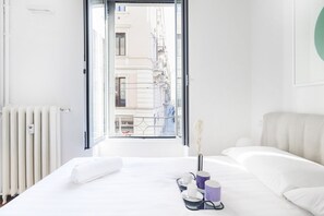 A hotel room with a bed, a radiator, a window, and a view of buildings outside. - Easylife - A touch of design in Porta Venezia (Milano)