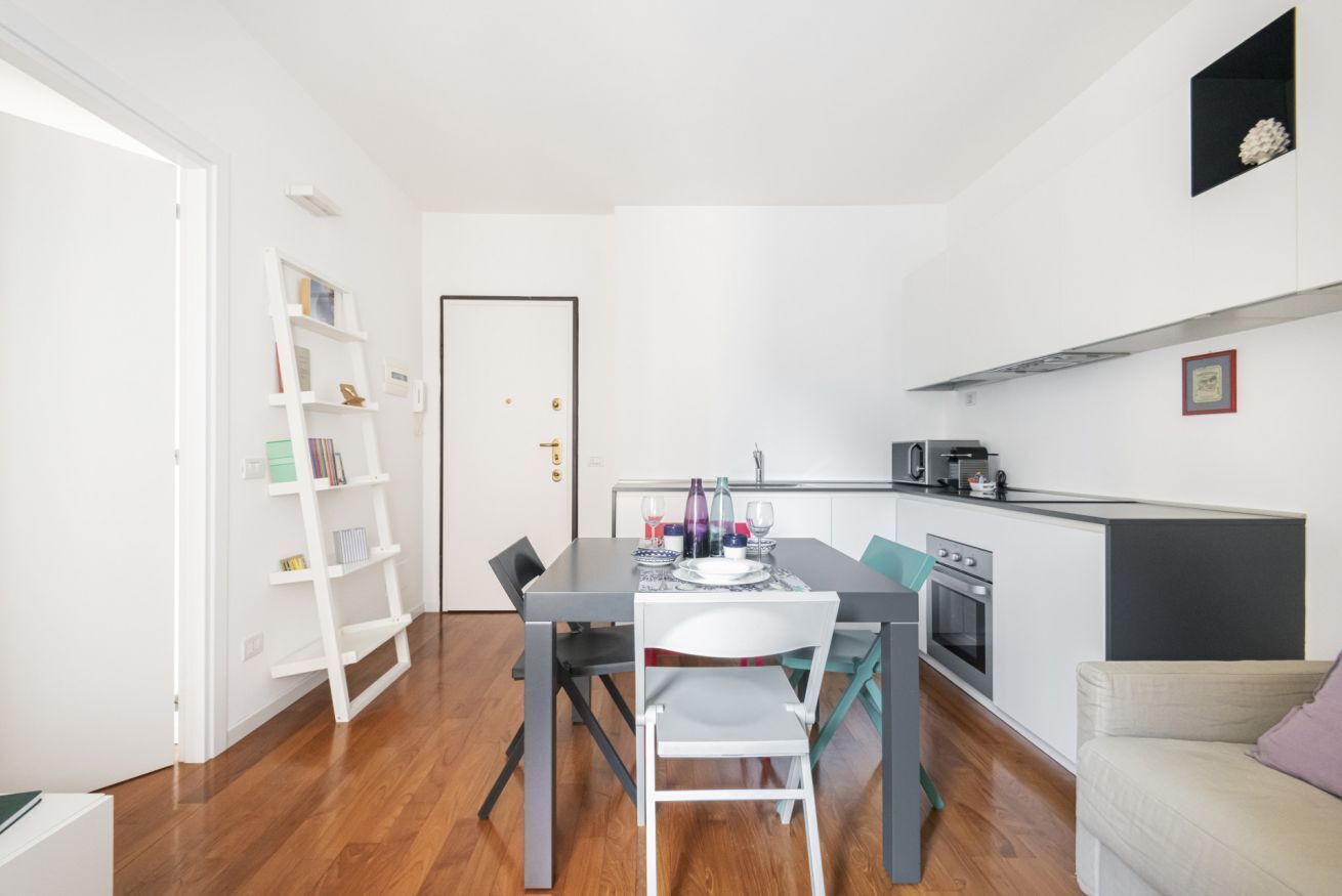 A compact living space with a dining area, kitchenette, and a bookshelf.