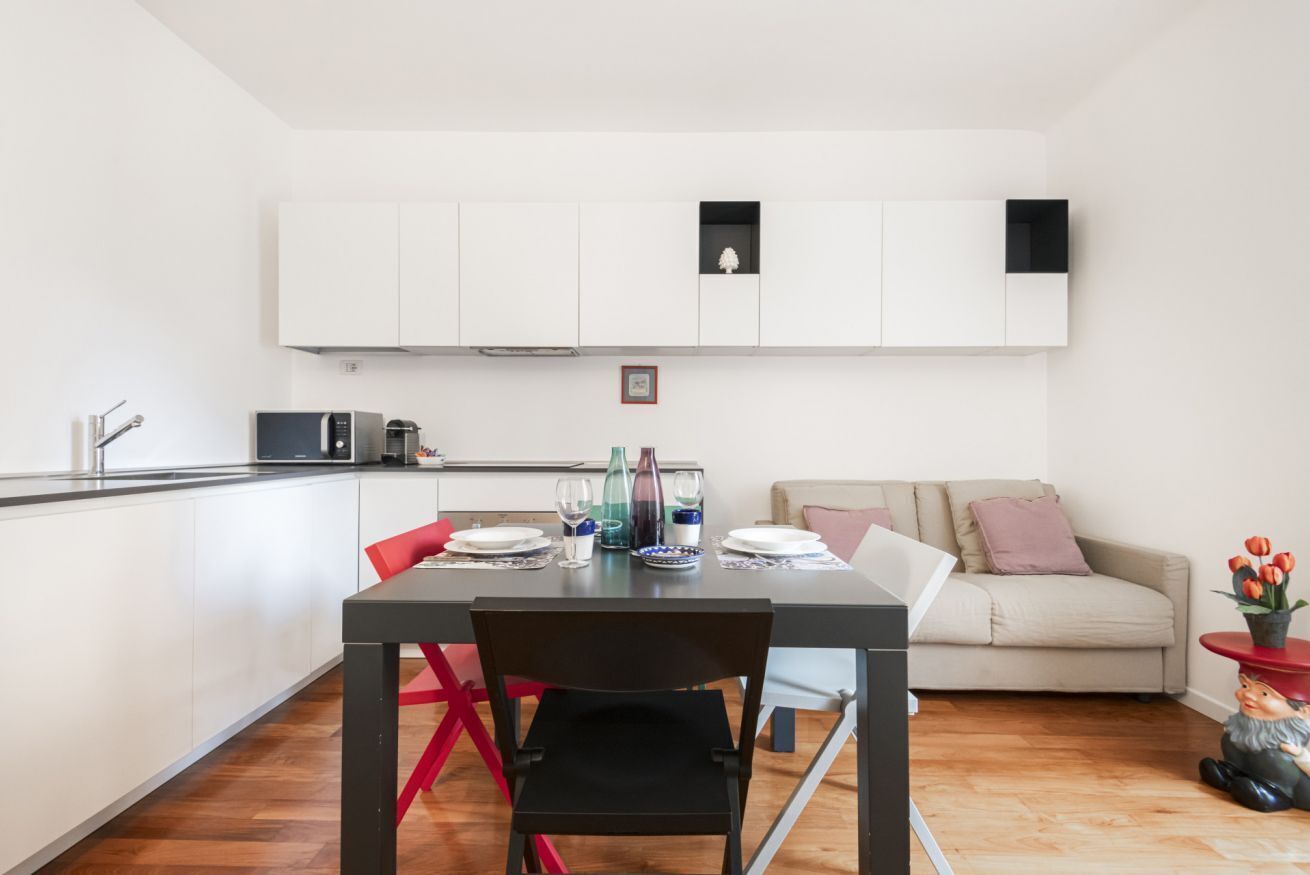 Eine moderne Küche mit weißen Schränken, einem Esstisch mit roten Stühlen und einem Sofa im Wohnbereich.