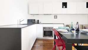 A modern kitchen with white cabinets, a built-in oven, and a dining area with a table and chairs. - Easylife - A touch of design in Porta Venezia (Milano)