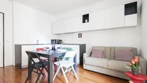 A modern kitchen with white cabinets, a dining table with chairs, and a sofa in a living area. - Easylife - A touch of design in Porta Venezia (Milano)